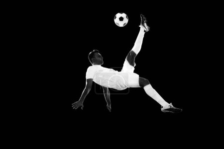 Photo for Dynamic image of motivated male soccer playing in motion, training, hitting ball and falling down on lack background. Monochrome. Concept of professional sport, game, competition, tournament, action - Royalty Free Image