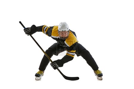 Foto de Hombre altamente concentrado, jugador de hockey con casco y uniforme de protección de pie en posición con palo durante el juego aislado sobre fondo blanco. Concepto de deporte, competición, torneo - Imagen libre de derechos