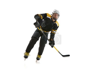 Téléchargez les photos : Jeune homme compétitif, joueur de hockey en uniforme noir, jouant isolé sur fond blanc. Concept de sport professionnel, compétition, jeu, tournoi, mode de vie actif - en image libre de droit