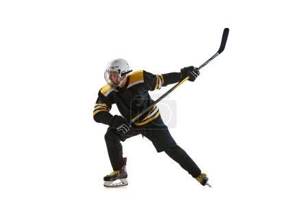 Téléchargez les photos : Jeune homme compétitif, joueur de hockey en uniforme noir, jouant isolé sur fond blanc. Concept de sport professionnel, compétition, jeu, tournoi, mode de vie actif - en image libre de droit