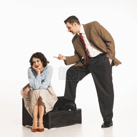 Téléchargez les photos : Homme en costume gesticulant à la femme assise sur le sol, suggérant confrontation, dispute. Jeune femme élégante exprimant son désaccord. Concept de rétro et vintage, mode, relation, émotions humaines - en image libre de droit