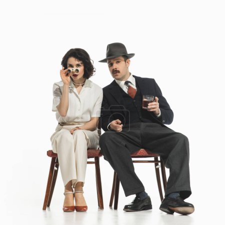 Photo for Elegant stylish couple, man and woman in classical suits with binoculars sitting and watching performance. Concept of retro and vintage, fashion, romance, relationship, entertainment - Royalty Free Image