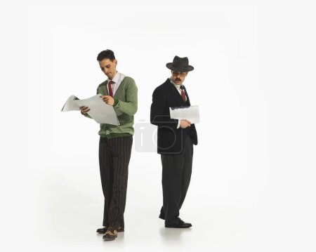 Téléchargez les photos : Deux hommes en tenue rétro avec des journaux isolés sur fond blanc. Homme regardant avec un intérêt caché sur les papiers. Concept de rétro et vintage, mode, business - en image libre de droit