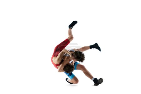 Athletes in motion. Young men in blue and red uniform, wrestlers training, demonstrating strength isolated on white background. Combat sport, martial arts, competition, tournament, athleticism concept