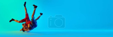 Foto de Dos jóvenes atletas masculinos en movimiento, luchando, luchando contra el fondo azul en luz de neón. Concepto de deporte de combate, artes marciales, competición, torneo, atletismo. Banner para anuncio, espacio para texto - Imagen libre de derechos