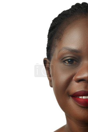 Téléchargez les photos : Portrait mi-visage de belle femme africaine aux lèvres rouges, la peau immaculée souriante, posant isolée sur fond de studio blanc. Concept de beauté naturelle, soin de la peau et du corps, cosmétologie, cosmétique - en image libre de droit