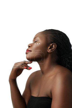 Téléchargez les photos : Routines quotidiennes de soins de la peau. Portrait de femme africaine élégante avec crème faciale sur les joues posant isolée sur fond de studio blanc. Concept de beauté naturelle, soin de la peau et du corps, cosmétologie, cosmétique - en image libre de droit