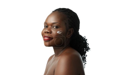 Téléchargez les photos : Natural skincare remedies. Beautiful African woman with face cream on cheeks posing isolated on white studio background. Concept of natural beauty, skin and body care, cosmetology, cosmetics - en image libre de droit