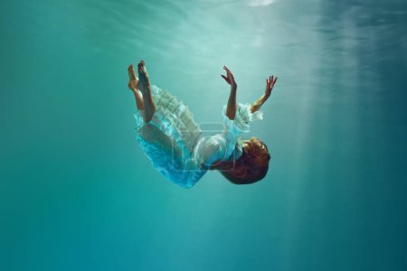 Foto de Caer en lo desconocido. Surrealista escena creativa bajo el agua con elegante mujer joven levitando con gracia bajo el agua. Concepto de surrealismo, belleza, misterio y fantasía, libertad - Imagen libre de derechos