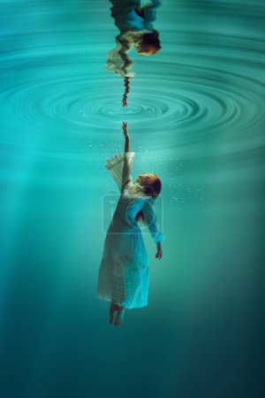 Photo for Finding inner self and truth. Poetic underwater scene with elegant young girl reaching out towards distorted reflection on waters surface. Concept of surrealism, beauty, mystery and fantasy, freedom - Royalty Free Image