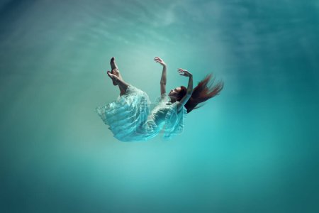 Photo for Magic and mystery hidden beneath the ocean. Elegant young girl levitating underwater, finding peace and calmness. Concept of surrealism, beauty, mystery and fantasy, freedom - Royalty Free Image