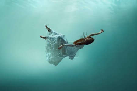 Photo for Magic and mystery hidden beneath the ocean. Elegant young girl levitating underwater, finding peace and calmness. Concept of surrealism, beauty, mystery and fantasy, freedom - Royalty Free Image