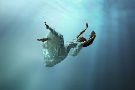 Photo for Angelic young girl in tender dress immersed in a world of tranquility and freedom. Girl levitating underwater with calmness. Concept of surrealism, beauty, mystery and fantasy, freedom - Royalty Free Image