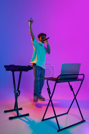 Téléchargez les photos : Jeune DJ, immergé dans la musique, mélange des pistes avec précision sur mixeur DJ, créant une atmosphère électrique sur fond dégradé rose violet en néon. Concept de musique, performance, concert en direct - en image libre de droit