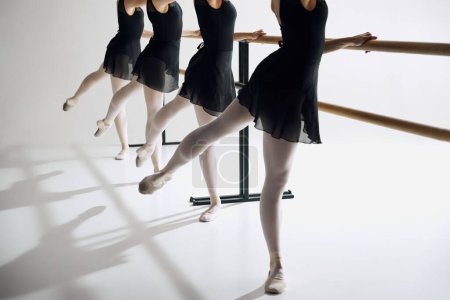 Téléchargez les photos : Élégance sur pointe. Image recadrée d'une danseuse de ballet debout dans une rangée à la barre, pratiquant sur fond de studio gris. Concept de ballet, art, studio de danse, style classique, jeunesse - en image libre de droit