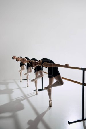 Téléchargez les photos : Danseurs de ballet synchronisés. Élégantes jeunes filles, ballerines debout à la barre et pratiquant sur fond de studio gris. Concept de ballet, art, studio de danse, style classique, jeunesse - en image libre de droit