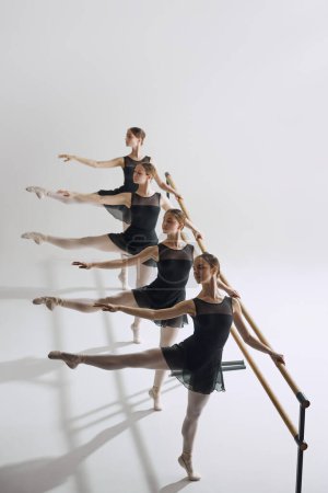 Téléchargez les photos : Symétrie et grâce dans le ballet. Quatre filles flexibles, danseuses de ballet debout à la barre et s'entraînant sur fond de studio gris. Concept de ballet, art, studio de danse, style classique, jeunesse - en image libre de droit