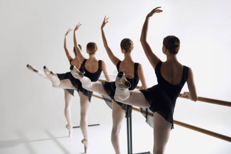 Téléchargez les photos : Adolescentes, danseuses de ballet pratiquant à la barre, focalisant l'attention sur la technique et l'élégance sur fond de studio gris. Concept de ballet, art, studio de danse, style classique, jeunesse - en image libre de droit