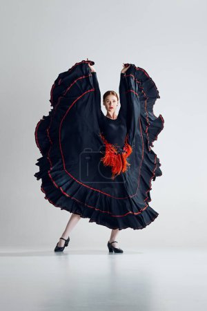 Photo for Like a butterfly. Elegant woman, flamenco dancer n striking black and red dress performing with passion, dancing against grey studio background. Concept of art of movement, classical dance, beauty - Royalty Free Image