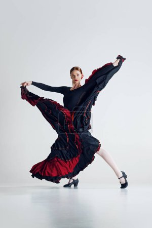 Photo for Focused and fiery flamenco dancer, elegant woman performing traditional Spanish cultural dance against grey studio background. Concept of art of movement, classical dance, beauty, festival - Royalty Free Image