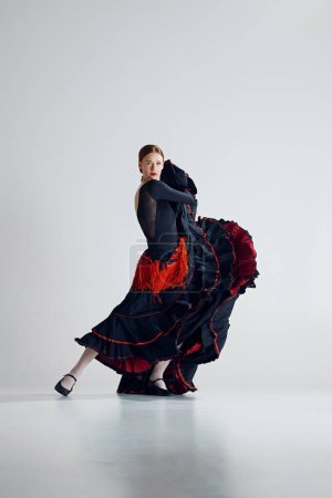 Photo for Captivating flamenco performance. Passionate and artistic woman in elegant dress dancing traditional Spanish dance against grey studio background. Concept of art of movement, classical dance, beauty - Royalty Free Image