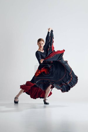 Téléchargez les photos : Grâce et passion. Femme élégante en robe noire et rouge frappante faisant de puissantes performances de danse flamenco sur fond de studio gris. Concept d'art du mouvement, danse classique, beauté, festival - en image libre de droit