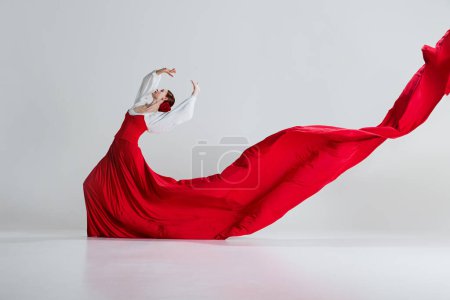 Téléchargez les photos : Femme élégante, danseuse de flamenco en robe rouge radieuse debout en pose dramatique, parfumée sur fond de studio gris. Esprit de danse. Concept d'art du mouvement, danse classique, beauté, festival - en image libre de droit