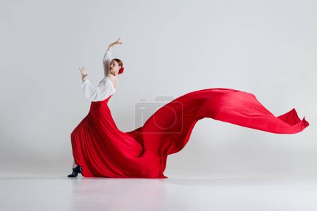 Téléchargez les photos : Passion. Danseuse en costume rouge frappant dansant le flamenco sur fond de studio gris. Moment de danse à couper le souffle. Concept d'art du mouvement, danse classique, beauté, festival - en image libre de droit