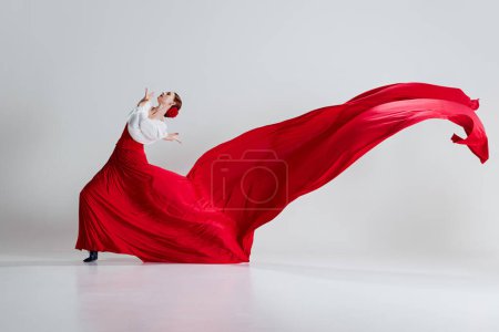 Téléchargez les photos : L'art du flamenco. Femme avec passion et élégance manifestant, exécutant la danse traditionnelle espagnole sur fond de studio gris. Concept d'art du mouvement, danse classique, beauté, festival - en image libre de droit