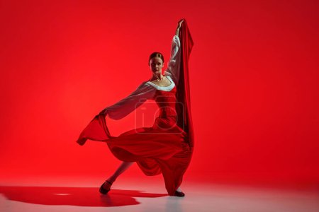 Foto de Bailarina de flamenco artística femenina mostrando pasión contra un fondo rojo llamativo. Elegante pose y falda fluida mostrando intensas emociones de baile. Concepto de arte del movimiento, danza clásica, belleza - Imagen libre de derechos