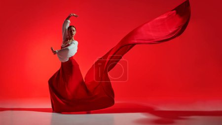 Photo for Passionate and elegant woman in vivid stage costume making creative performance against bright red background. Concept of art of movement, classical dance, beauty, festival - Royalty Free Image