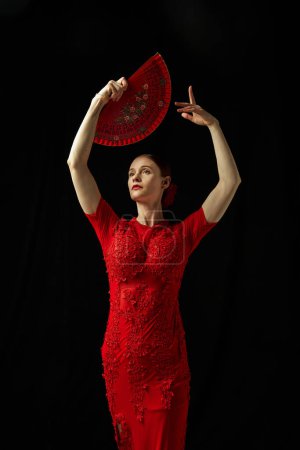 Photo for Creative portrait of elegant woman in red dress, flamenco dance posing against black background. Concept of art of movement, classical dance, beauty, festival - Royalty Free Image
