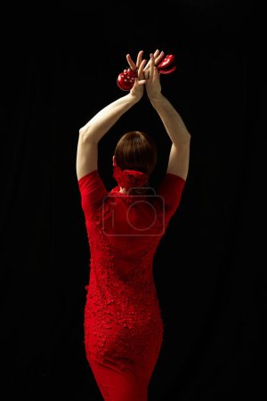 Téléchargez les photos : Moment figé dans le temps. Femme élégante en robe rouge debout avec castagnettes sur fond noir. Concept d'art du mouvement, danse classique, beauté, festival - en image libre de droit