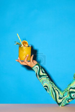 Photo for Female hand holding sweet and sour cocktail with orange juice and rosemary against blue background. Concept of alcohol and non-alcohol drink, party, holidays, bar, mix. Poster. Copy space for ad - Royalty Free Image