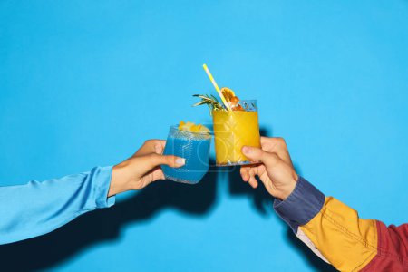 Foto de Gafas de mano masculinas y femeninas con cóctel agridulce azul y amarillo sobre fondo azul. ¡Salud! Concepto de bebida alcohólica y no alcohólica, fiesta, vacaciones. Cartel. Copiar espacio para anuncio - Imagen libre de derechos