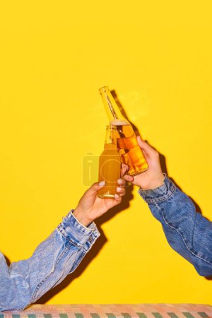 Téléchargez les photos : Mains mâles et femelles tenant des bouteilles avec de la bière et de la limonade, cliquetant sur un fond jaune vif. Concept de boisson alcoolisée et non alcoolisée, fête, vacances, bar, mix. Affiche. Espace de copie pour la publicité - en image libre de droit