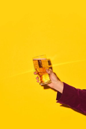 Foto de Mano masculina sosteniendo vidrio con cerveza lager sobre fondo amarillo brillante. Hora de la fiesta y refresco. Concepto de bebida alcohólica y no alcohólica, fiesta, vacaciones, bar, mezcla. Cartel. Copiar espacio para anuncio - Imagen libre de derechos
