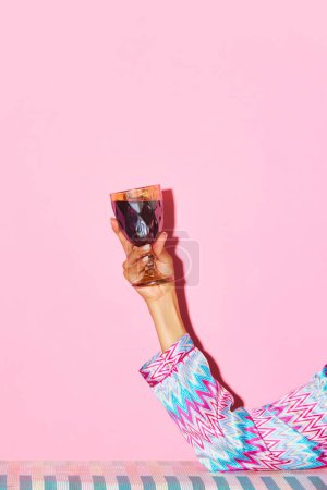 Foto de Mano femenina sosteniendo copa con vino tinto sobre fondo rosa. Brindis, celebración. Concepto de bebida alcohólica y no alcohólica, fiesta, vacaciones, bar, mezcla. Cartel. Copiar espacio para anuncio - Imagen libre de derechos