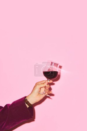 Foto de Mano masculina sosteniendo copa con vino tinto sobre fondo rosa. Evento de degustación. Concepto de bebida alcohólica y no alcohólica, fiesta, vacaciones, bar, mezcla. Cartel. Copiar espacio para anuncio - Imagen libre de derechos