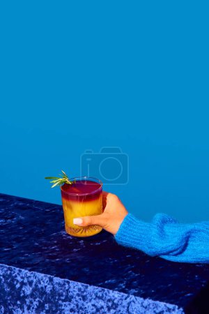 Foto de Mano femenina sosteniendo cóctel con jugo de naranja sobre fondo azul. Cóctel tradicional agrio de Nueva York. Concepto de bebida alcohólica y no alcohólica, fiesta, vacaciones, bar. Cartel. Copiar espacio para anuncio - Imagen libre de derechos