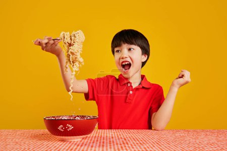 Photo for Cheerful emotional child playfully lifting noodles with fork against yellow background. Playful eating. Fast dinner ideas. Concept of food, childhood, emotions, meal, menu, pop art - Royalty Free Image