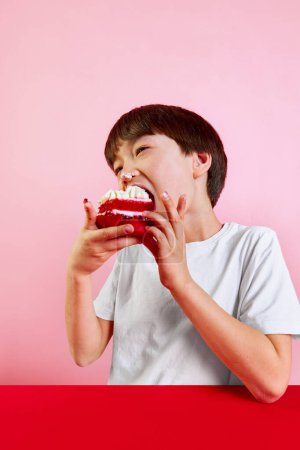 Photo for Sweet treat. Boy, kid enjoying delicious red velvet cake with cream and berries, making big bite against pink background. Concept of food, childhood, emotions, meal, menu, pop art - Royalty Free Image