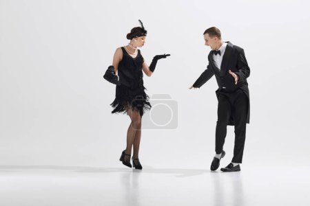 Photo for Black-and-white themed costume party. Beautiful young woman and handsome man dancing retro dance isolated over white studio background. Concept of art, retro and vintage, hobby, entertainment, 20s - Royalty Free Image