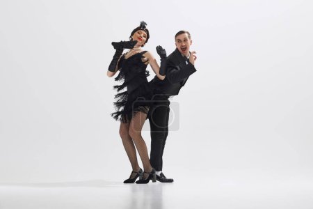 Photo for Young stylish man and woman dressed in 1920s attire perform lively Charleston dance isolated over white studio background. Concept of art, retro and vintage, hobby, entertainment, 20s - Royalty Free Image