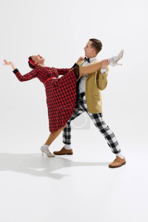 Téléchargez les photos : Moment ludique capturé entre un couple dansant, jeune homme beau et belle femme dansant énergiquement isolé sur fond de studio blanc. Concept d'art, rétro et vintage, divertissement - en image libre de droit