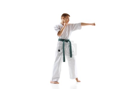 Foto de Adolescente concentrado, practicante de karate en postura defensiva, mostrando enfoque y preparación, practicando aislado en el fondo blanco del estudio. Concepto de deporte, artes marciales, deporte de combate - Imagen libre de derechos