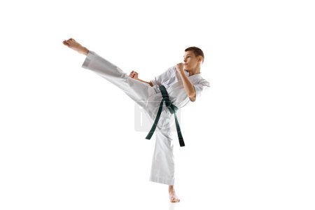 Photo for Teen boy, athlete practices karate moves, demonstrating skills and determination, practicing isolated on white studio background. Concept of sport, martial arts, combat sport, active lifestyle - Royalty Free Image