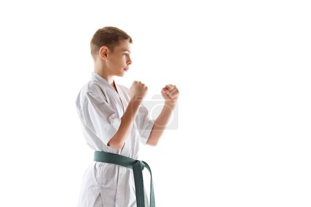 Photo for Concentrated teen boy, in defensive karate stance, showcasing focus and readiness, practicing isolated on white background. Concept of sport, martial arts, combat sport, healthy and active lifestyle - Royalty Free Image