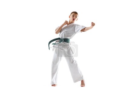 Foto de Niño adolescente enfocado, practicante de karate mostrando patada dinámica, ilustrando disciplina y poder aislado en fondo blanco estudio. Deportes, artes marciales, deporte de combate, salud, concepto de estilo de vida activo - Imagen libre de derechos