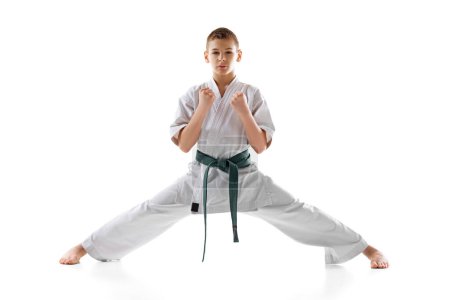 Foto de Niño adolescente, atleta de karate posando en kimono blanco con cinturón verde con enfoque y determinación aislados en el fondo blanco del estudio. Concepto de deporte, artes marciales, deporte de combate, estilo de vida activo - Imagen libre de derechos